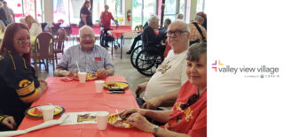 Valley View Village residents and staff enjoy a festive gathering, smiling and sharing a meal at a tailgate-themed event, surrounded by vibrant decorations.
